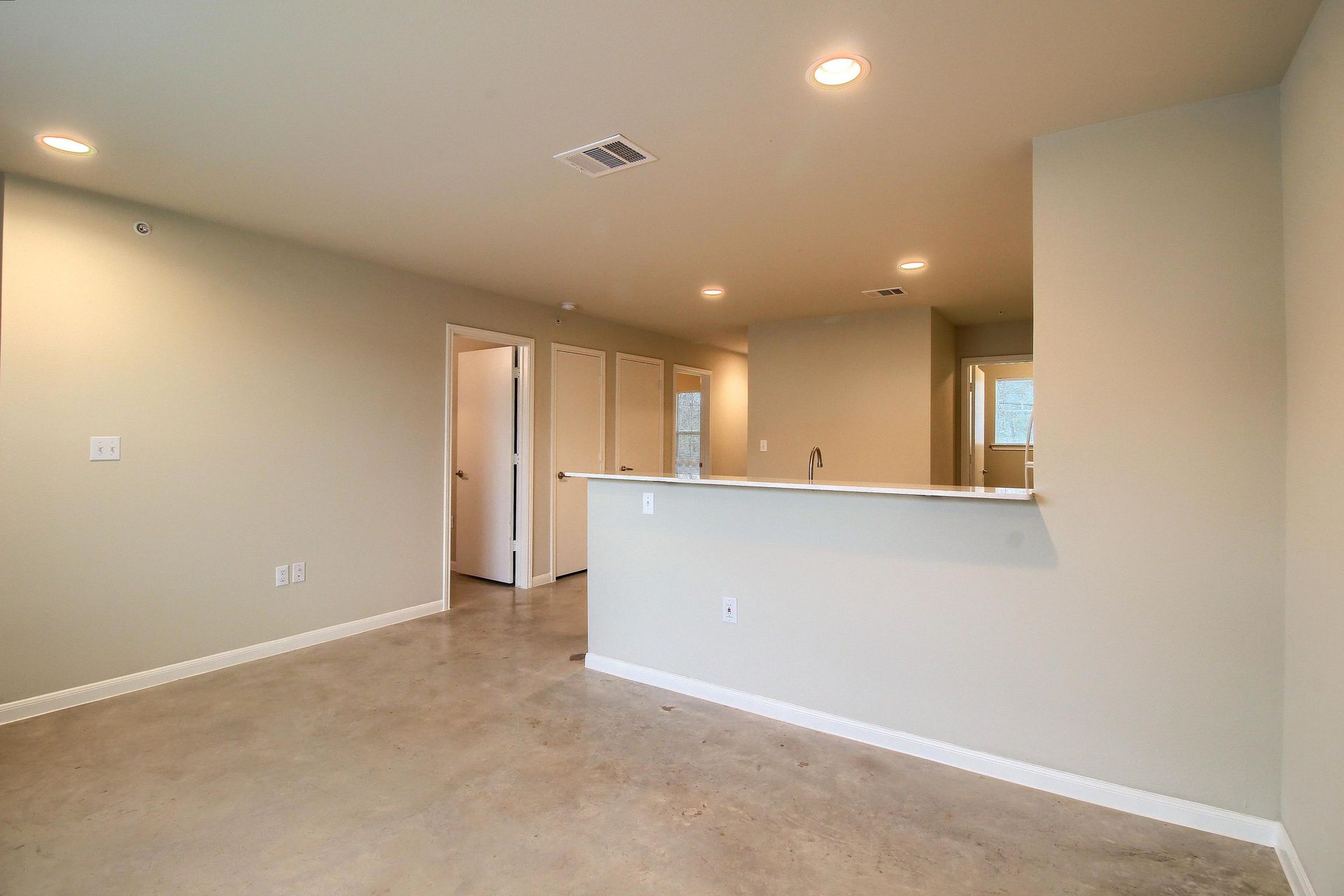 An empty living room with a kitchen in the background.
