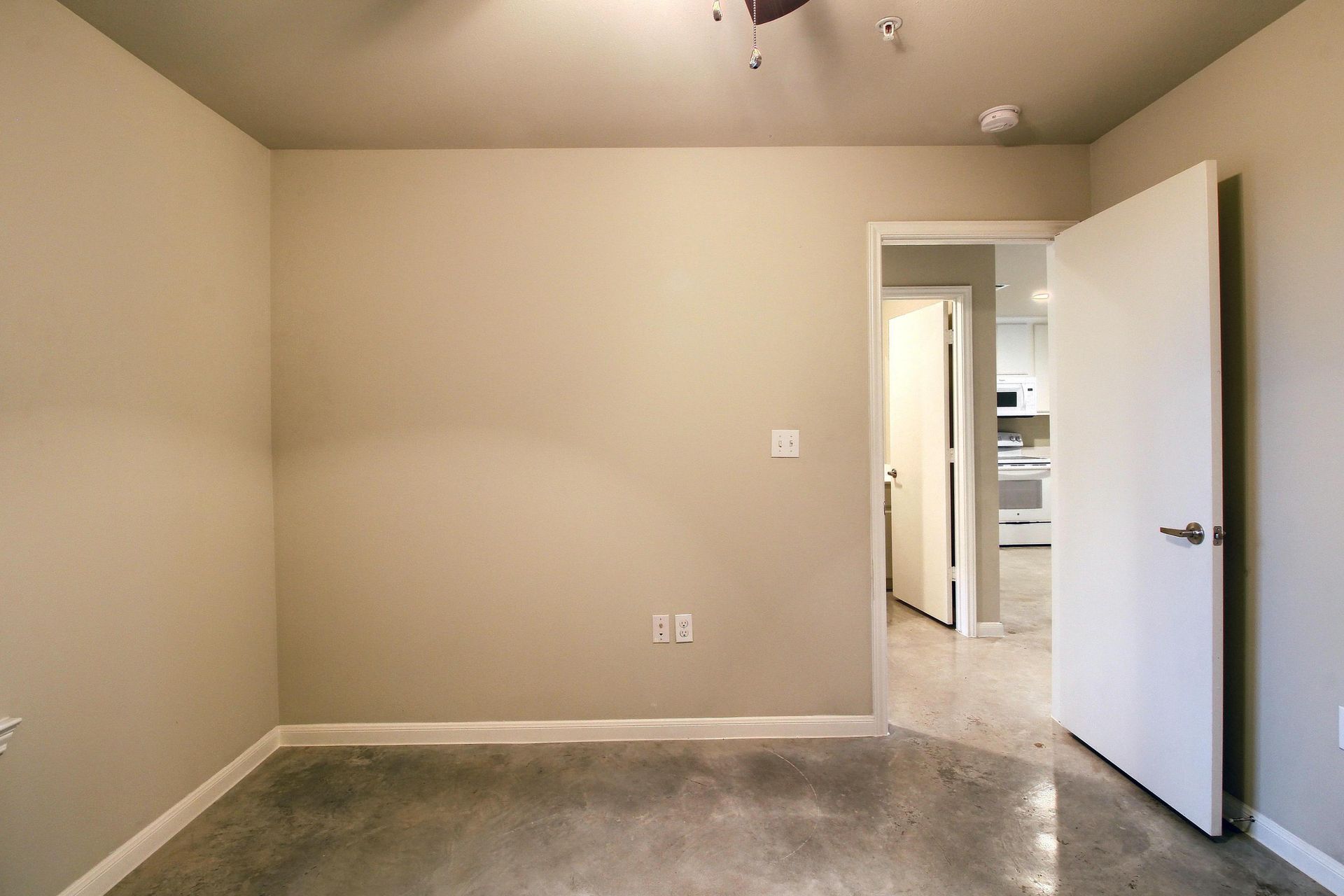 An empty room with a ceiling fan and a door leading to a kitchen.