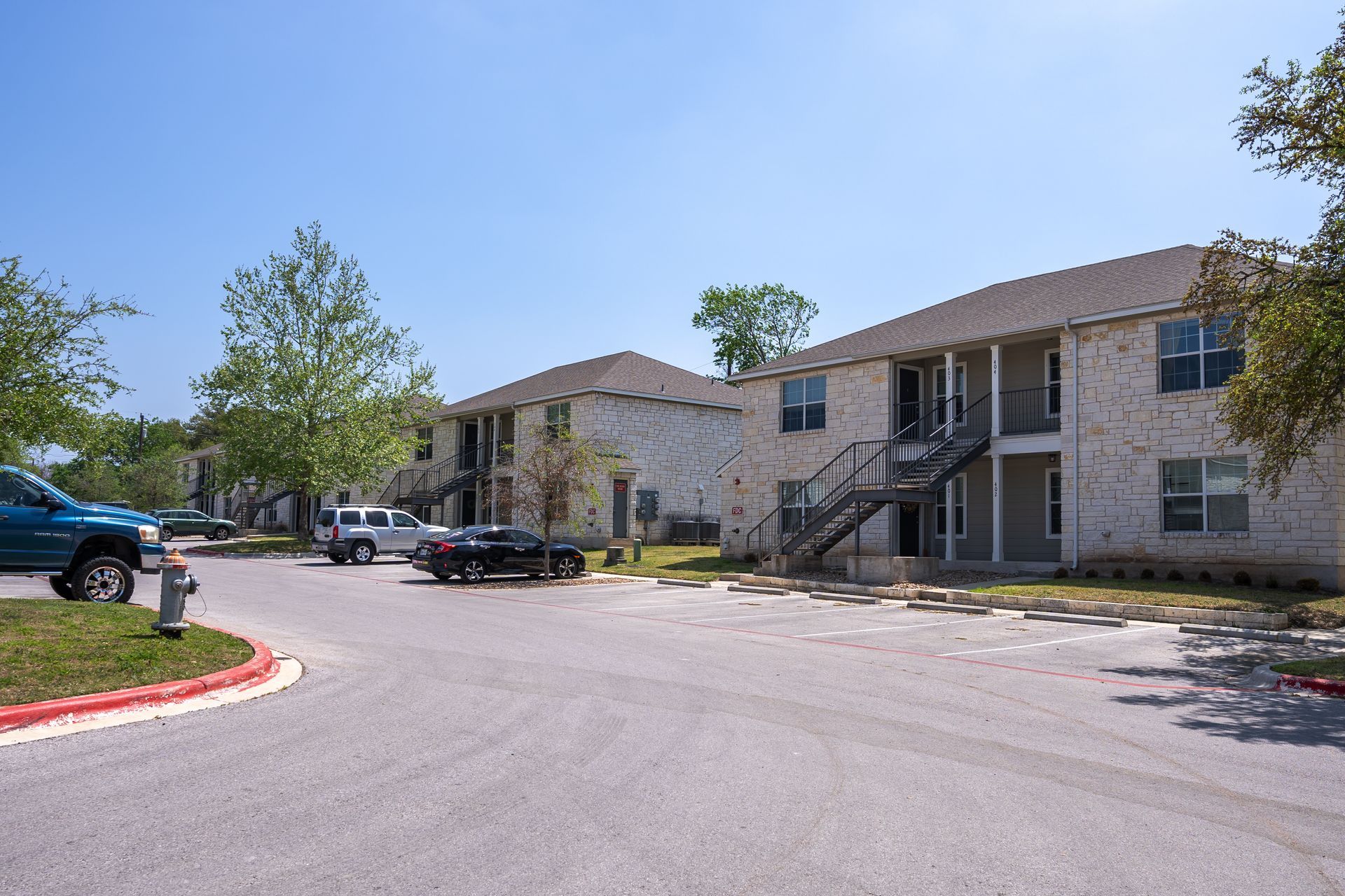 A row of apartment buildings with cars parked in front of them.