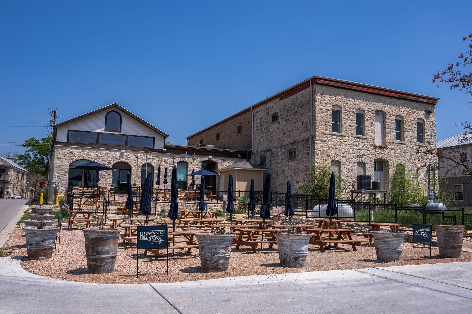 A large stone building with a lot of picnic tables and umbrellas in front of it.