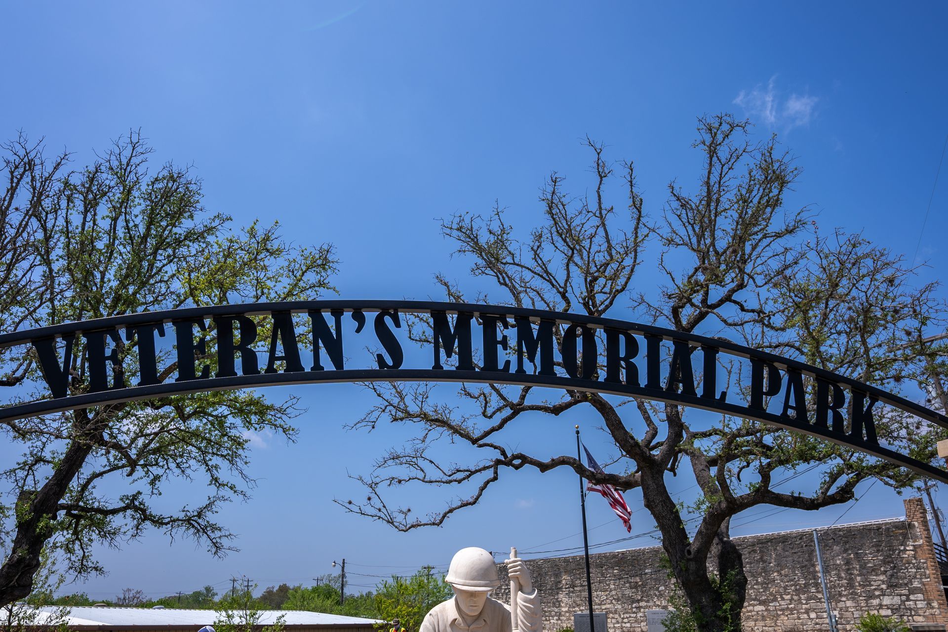 A statue of a man in a helmet is under a sign that says veteran 's memorial park.