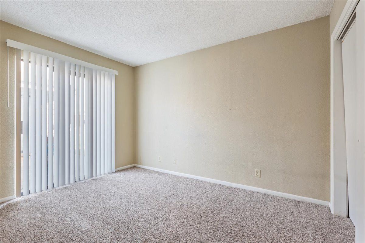 An empty living room with a sliding glass door and blinds.