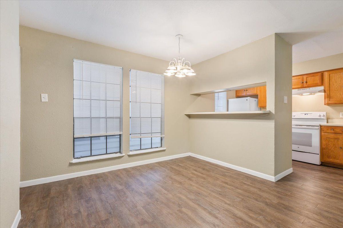 An empty living room with hardwood floors and a kitchen in the background.
