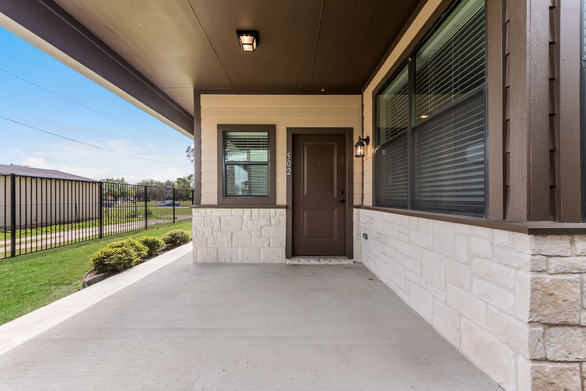The front porch of a house with a brick wall and a brown door.