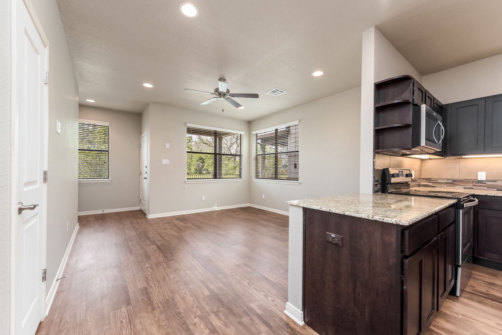A kitchen and living room in a house with hardwood floors and a ceiling fan.