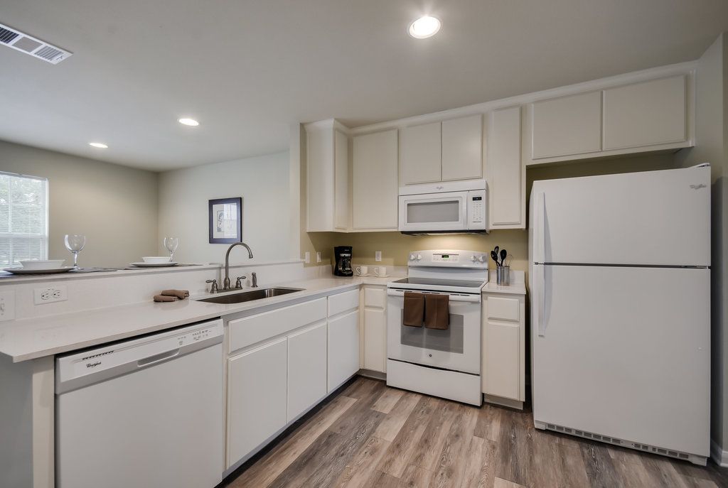 A kitchen with white cabinets , a refrigerator , a stove , and a sink.