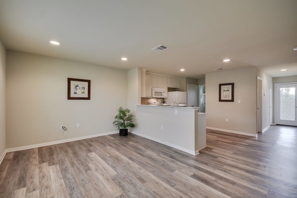 A living room with hardwood floors and a kitchen in the background.