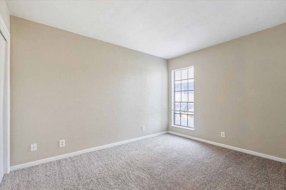 An empty bedroom with a window and a carpeted floor.