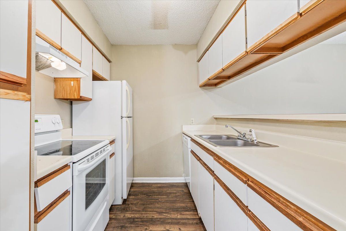 A kitchen with white cabinets , a stove , a refrigerator , and a sink.