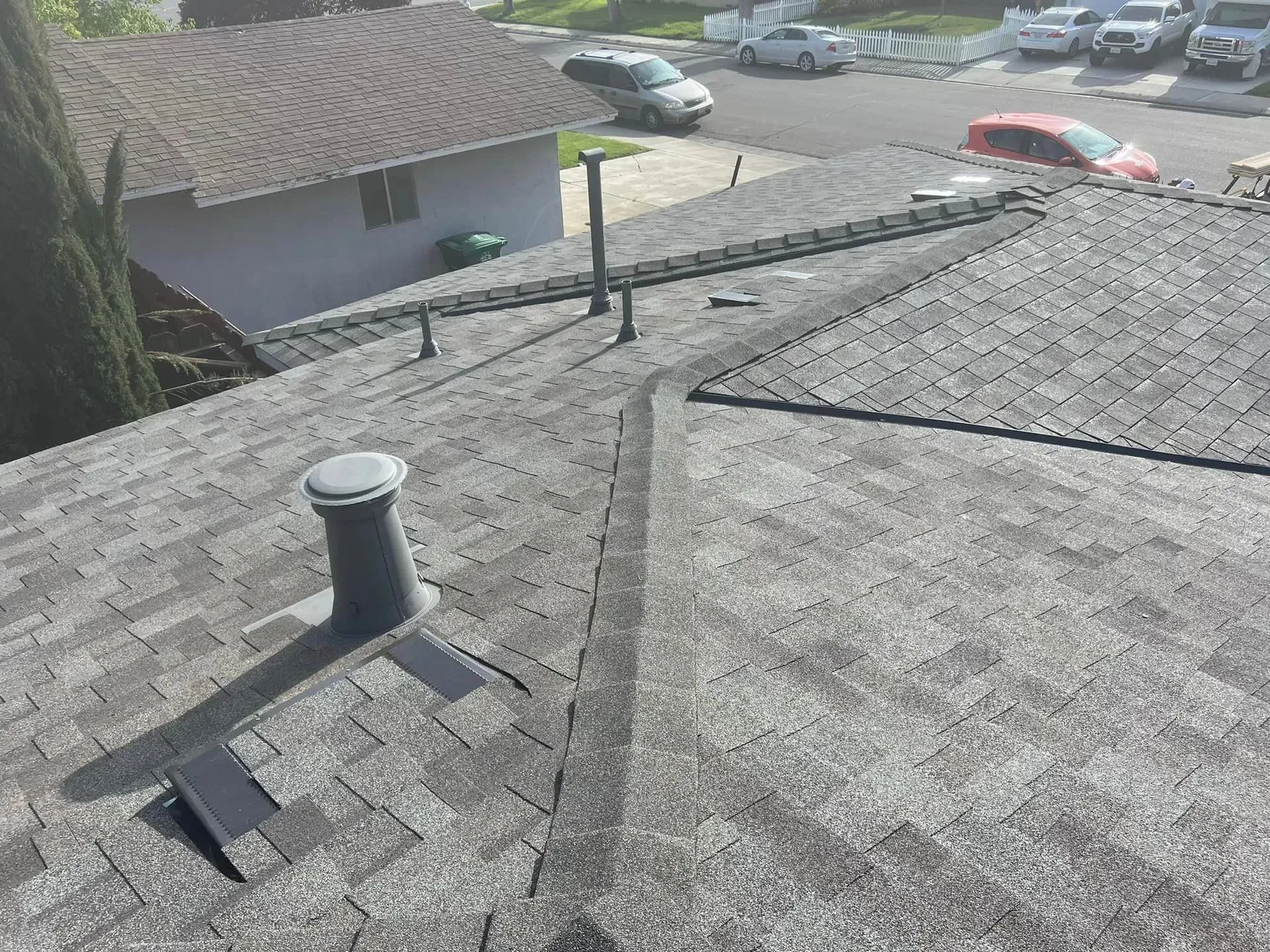 A roof with a vent on it and a car parked in the background.