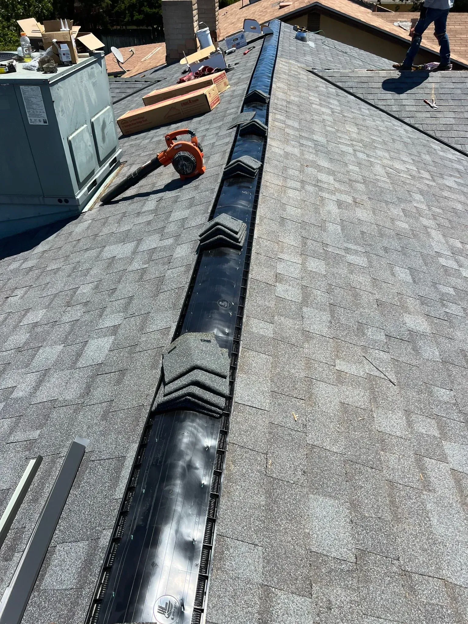A man is standing on top of a roof with a blower on it.