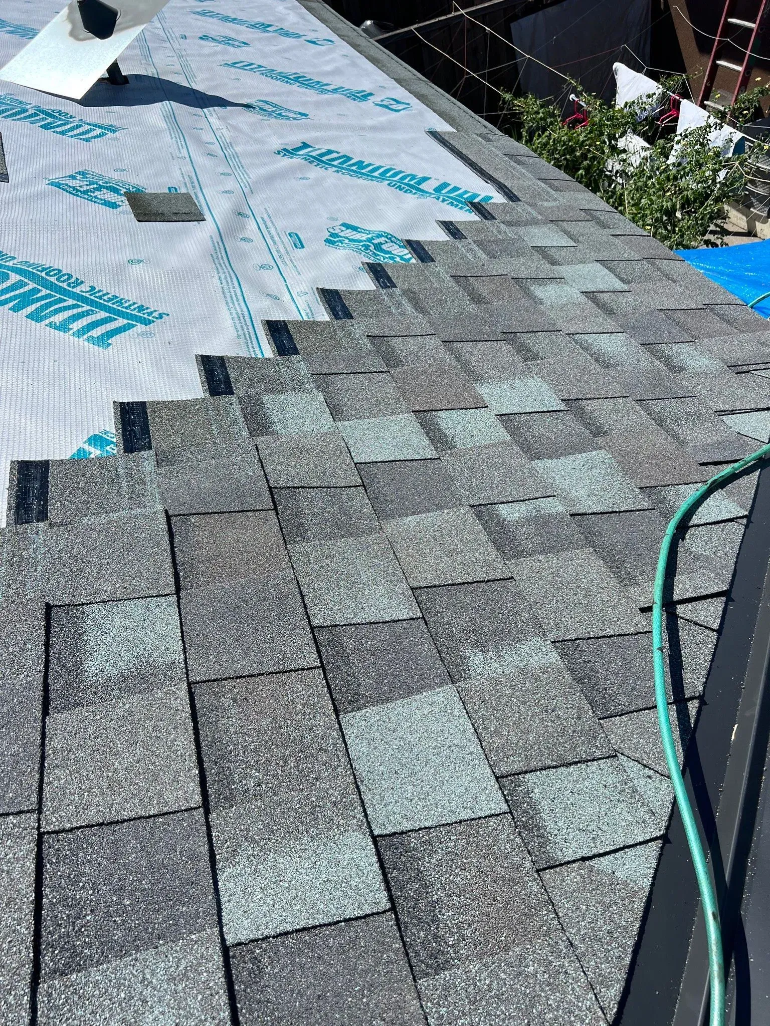 A roof with shingles being installed and a hose attached to it.