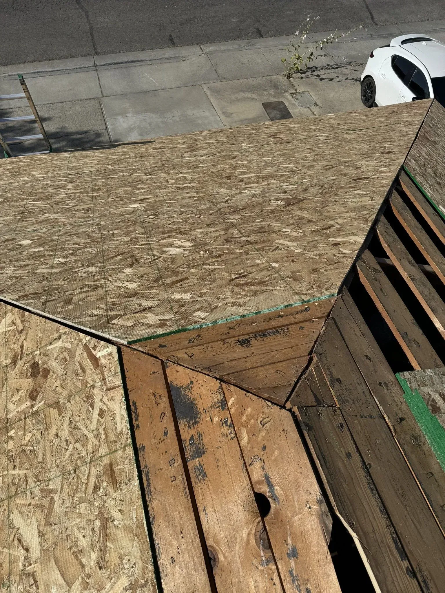 A white car is parked on the side of the road next to a wooden deck.