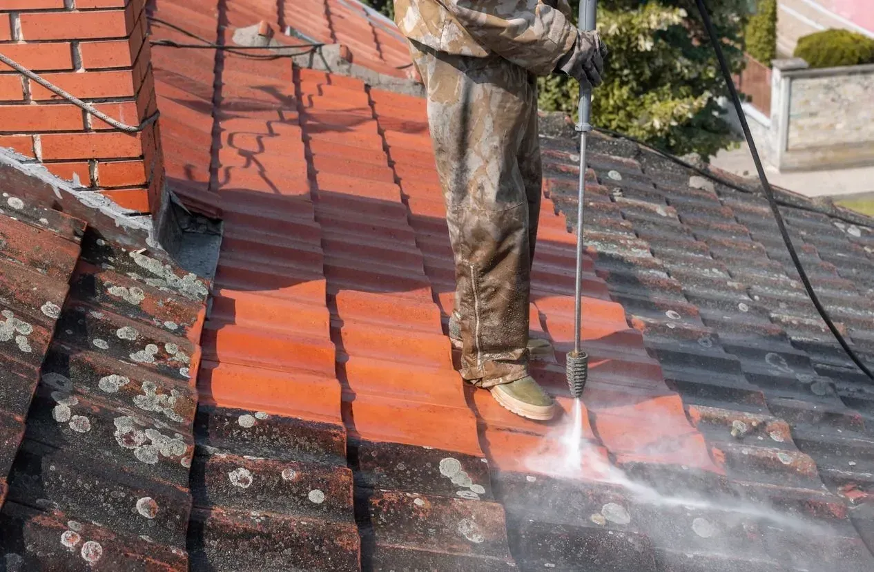 A man is cleaning a roof with a high pressure washer.