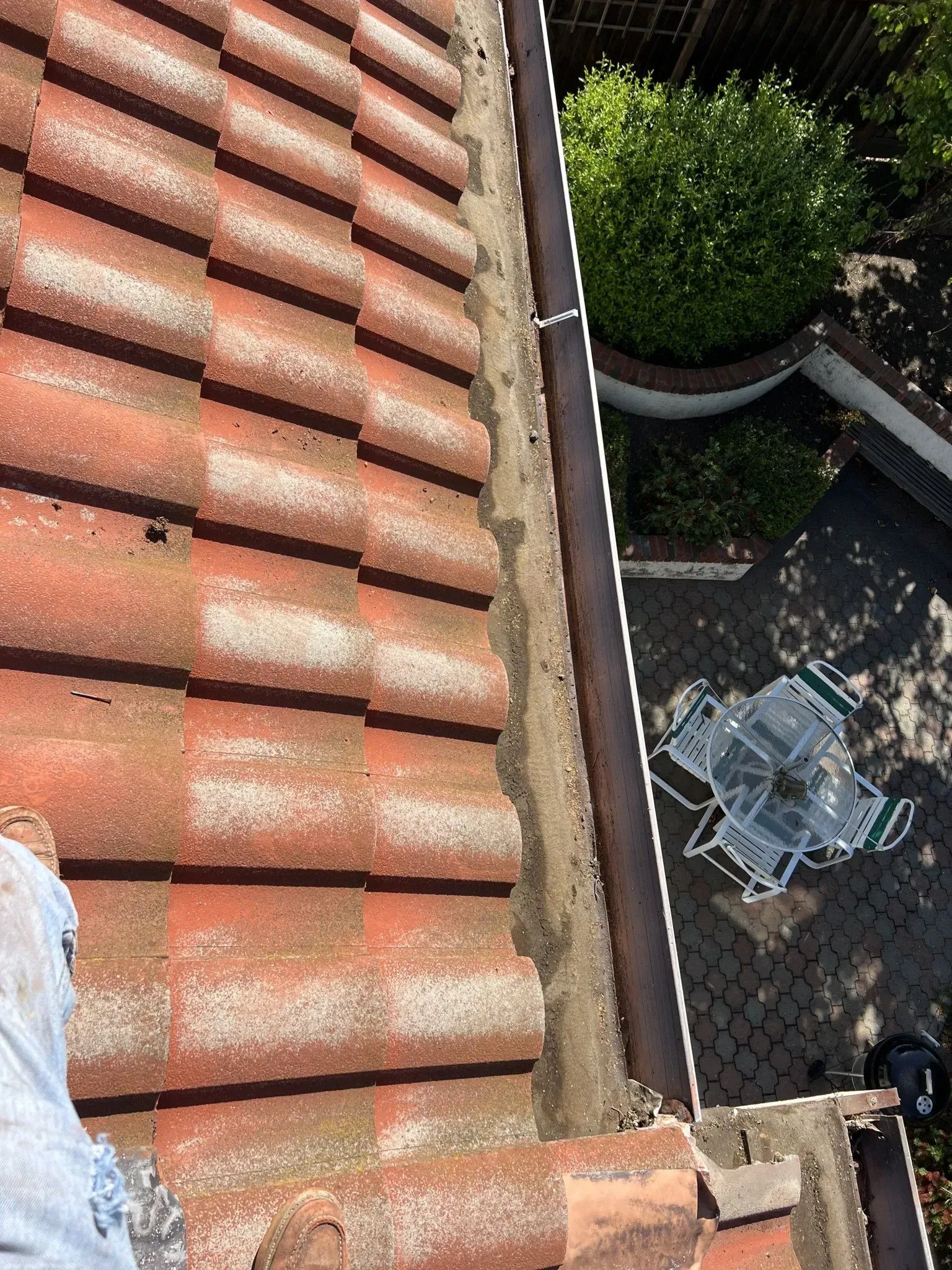 A person is standing on top of a tiled roof next to a gutter.