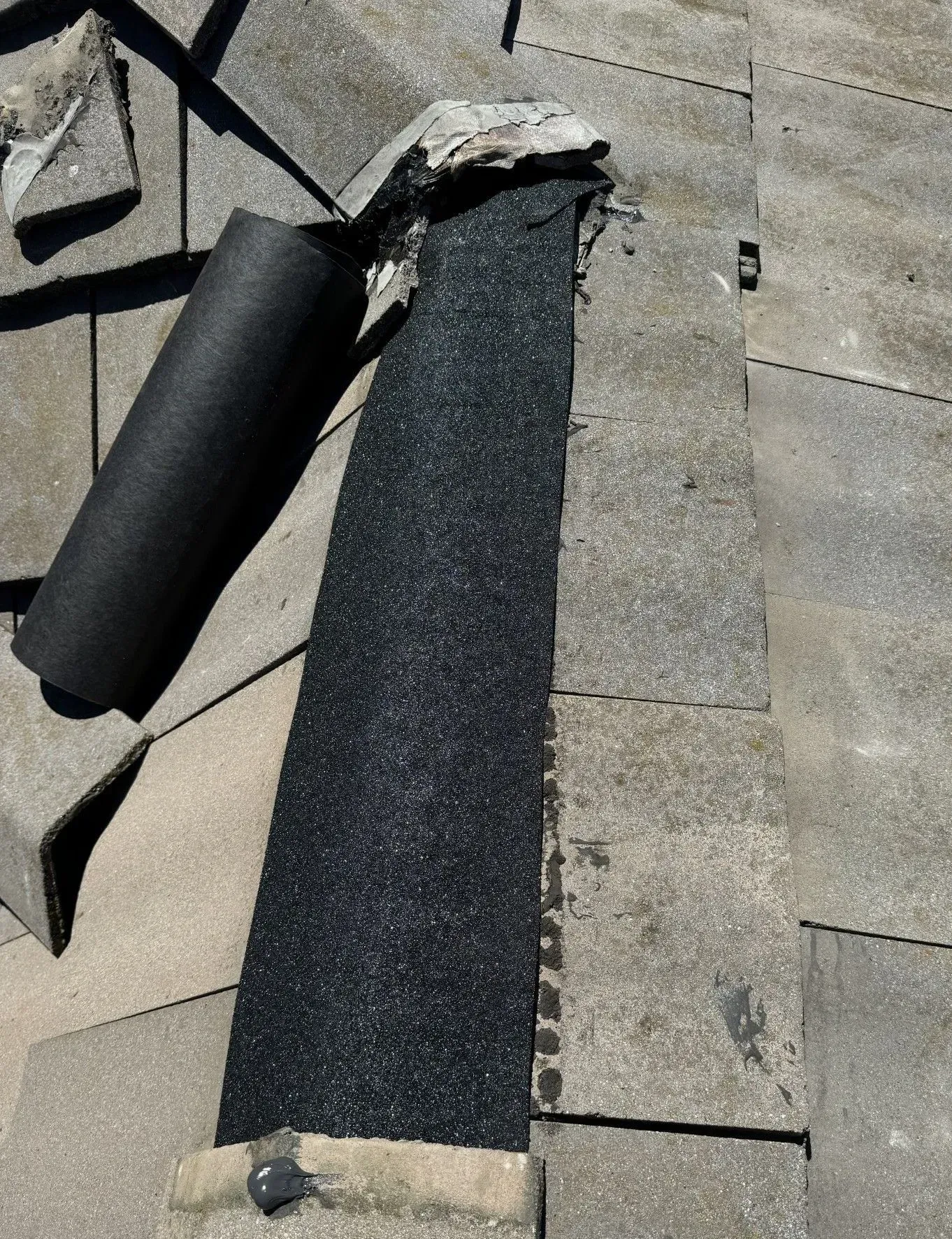 A roll of black rubber is laying on a concrete surface.