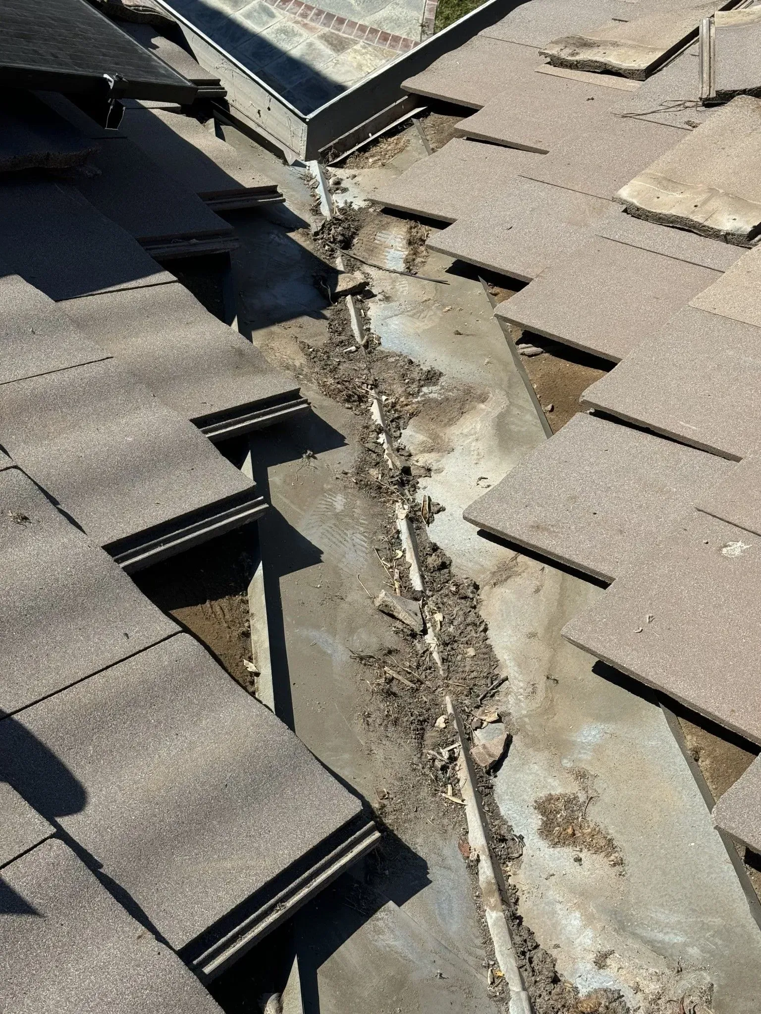 A close up of a roof with shingles missing and a hole in it.