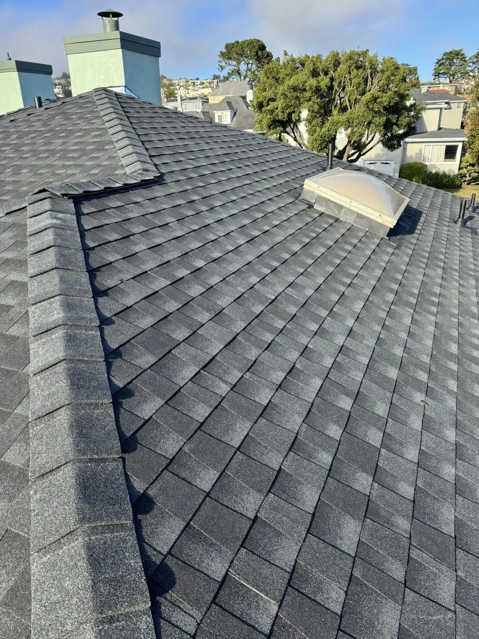 A close up of a roof with shingles and a skylight.