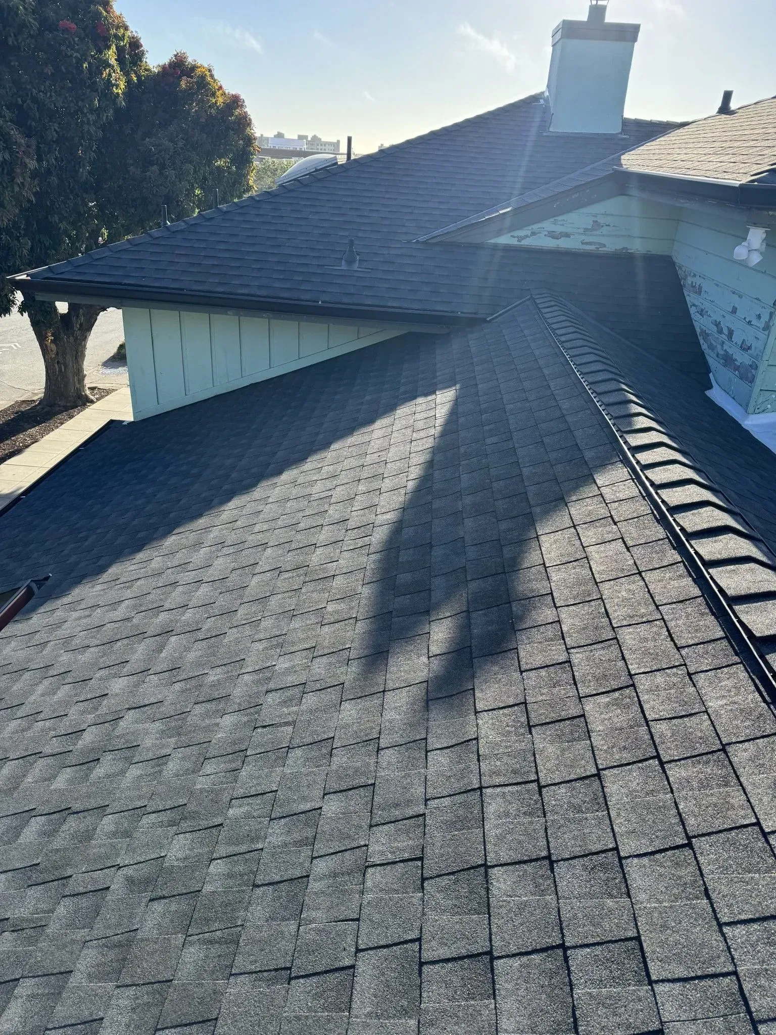 A close up of a roof with a chimney and a tree in the background.