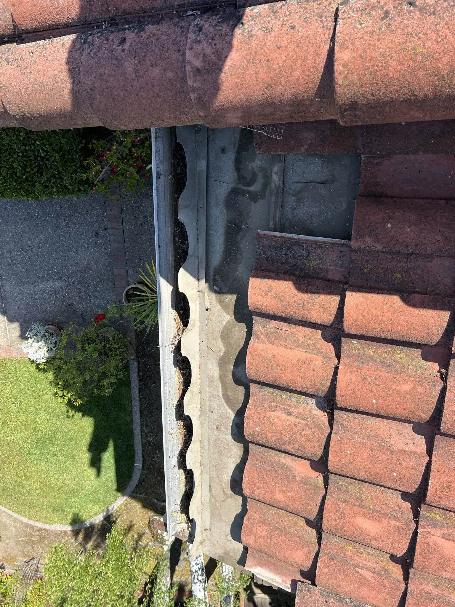 An aerial view of a roof with red tiles and a gutter.