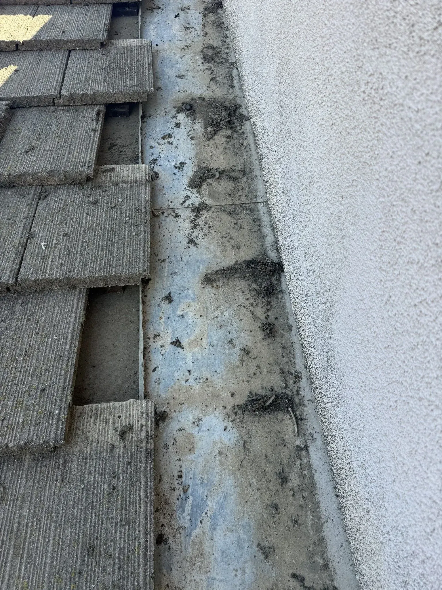 A close up of a gutter on a roof with shingles on it.