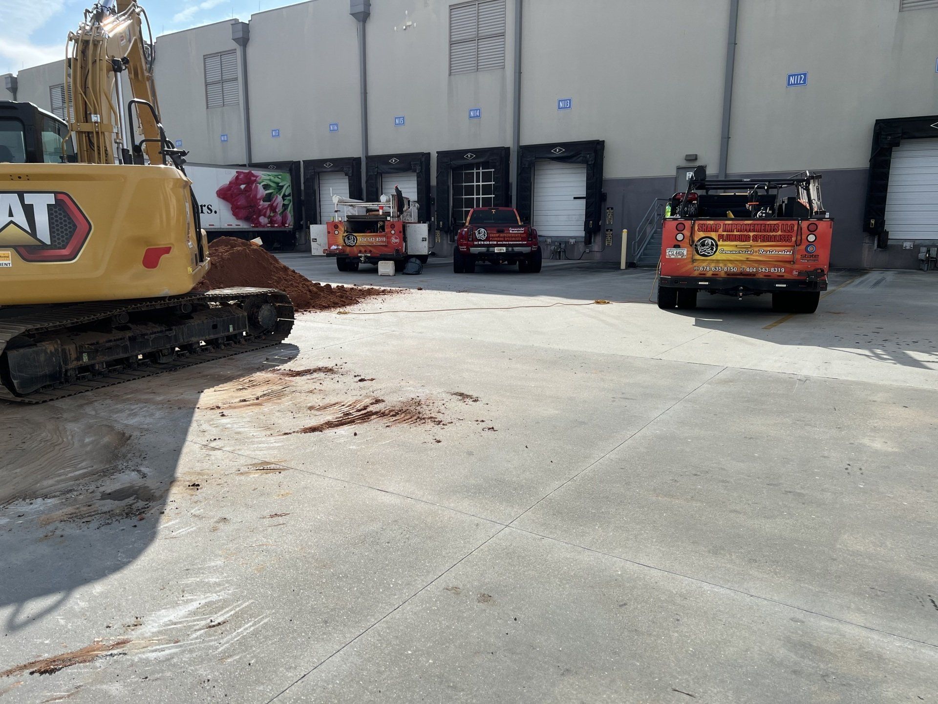 A cat excavator is digging a hole in a parking lot