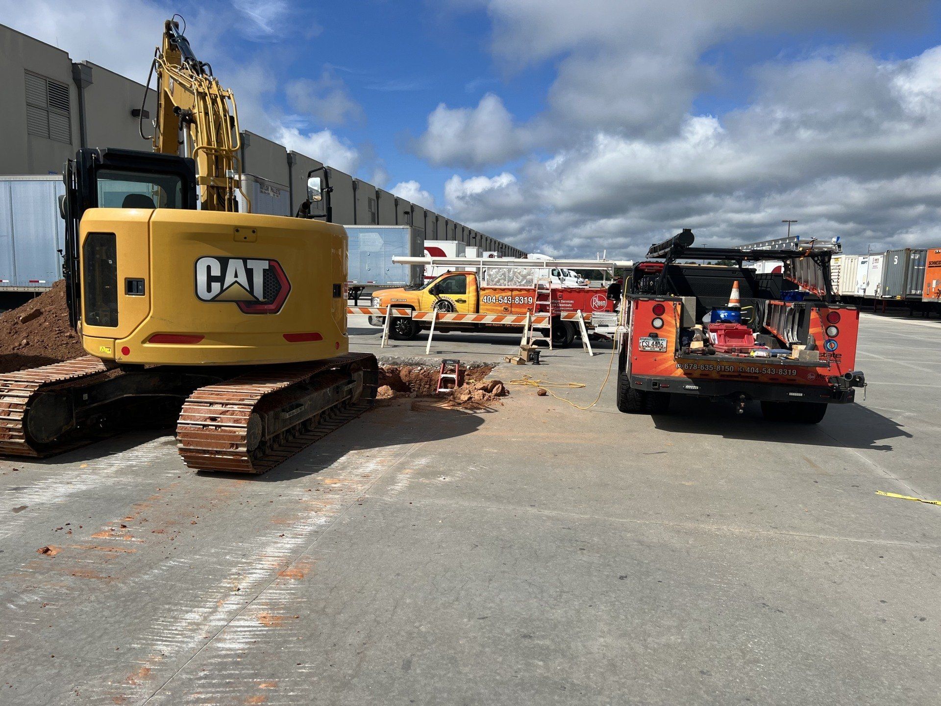 A cat excavator is parked in a parking lot next to a fire truck.