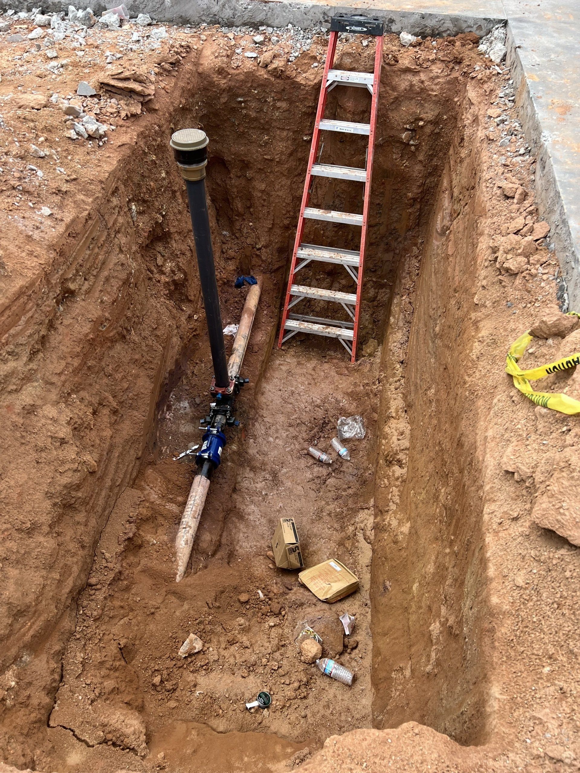 A ladder is sitting in a hole in the ground next to a pipe.