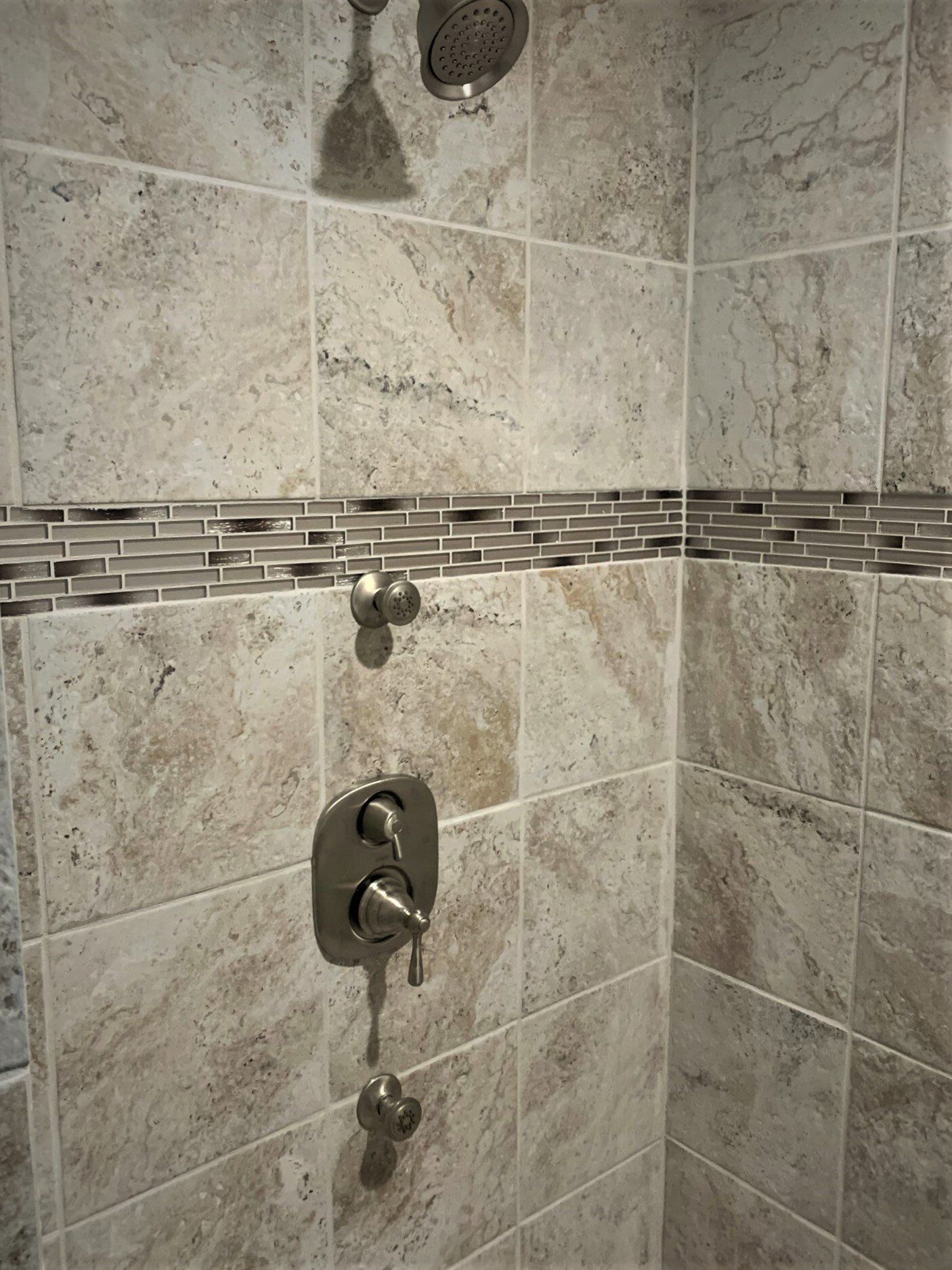 A shower with tile walls and a stainless steel shower head