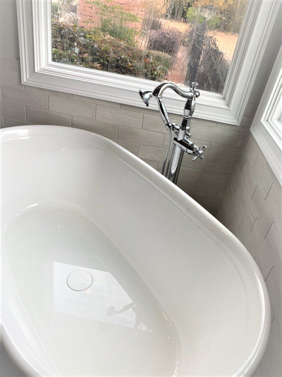 A white bathtub is sitting next to a window in a bathroom.