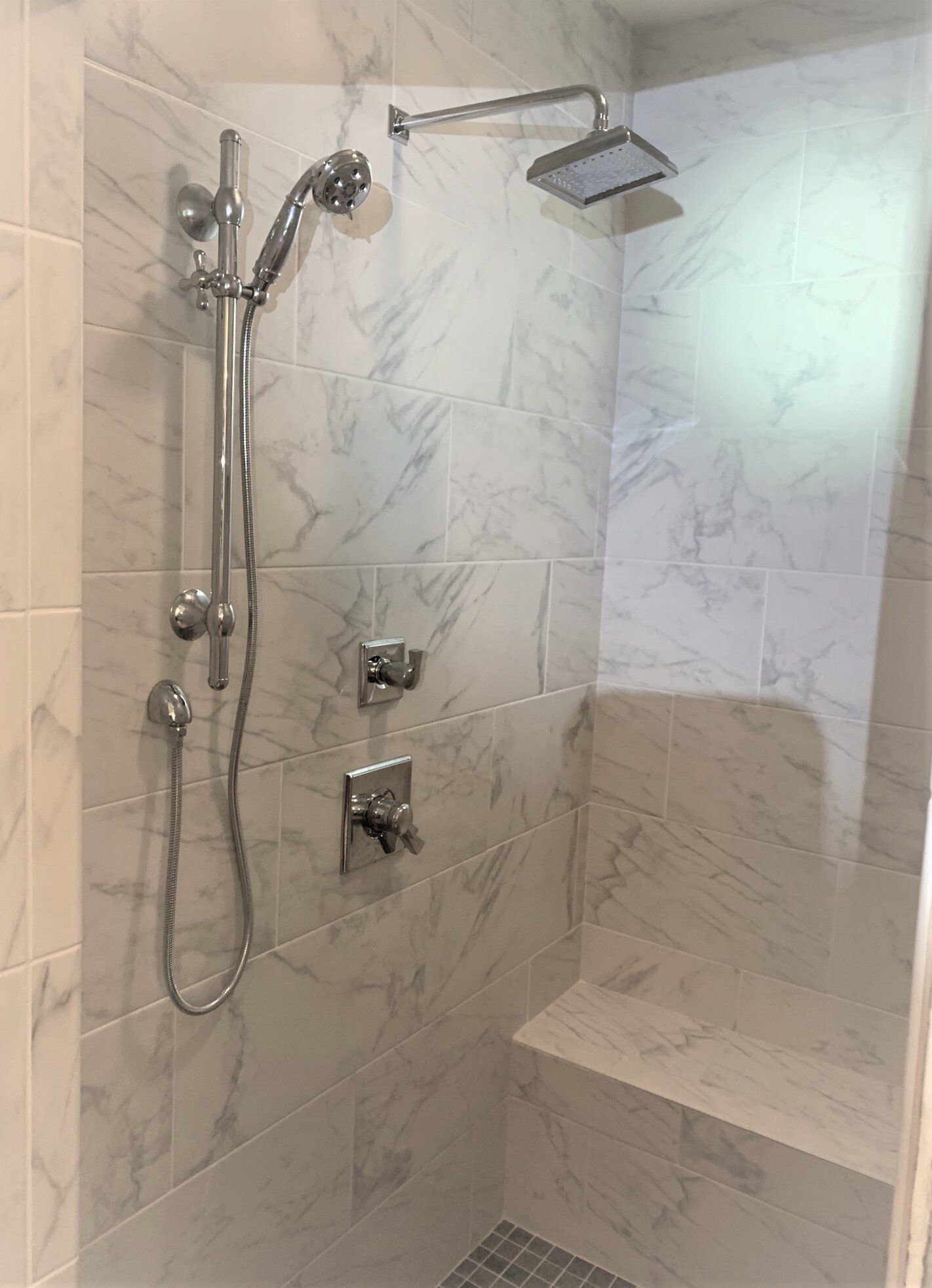 A shower with a bench and a shower head in a bathroom.