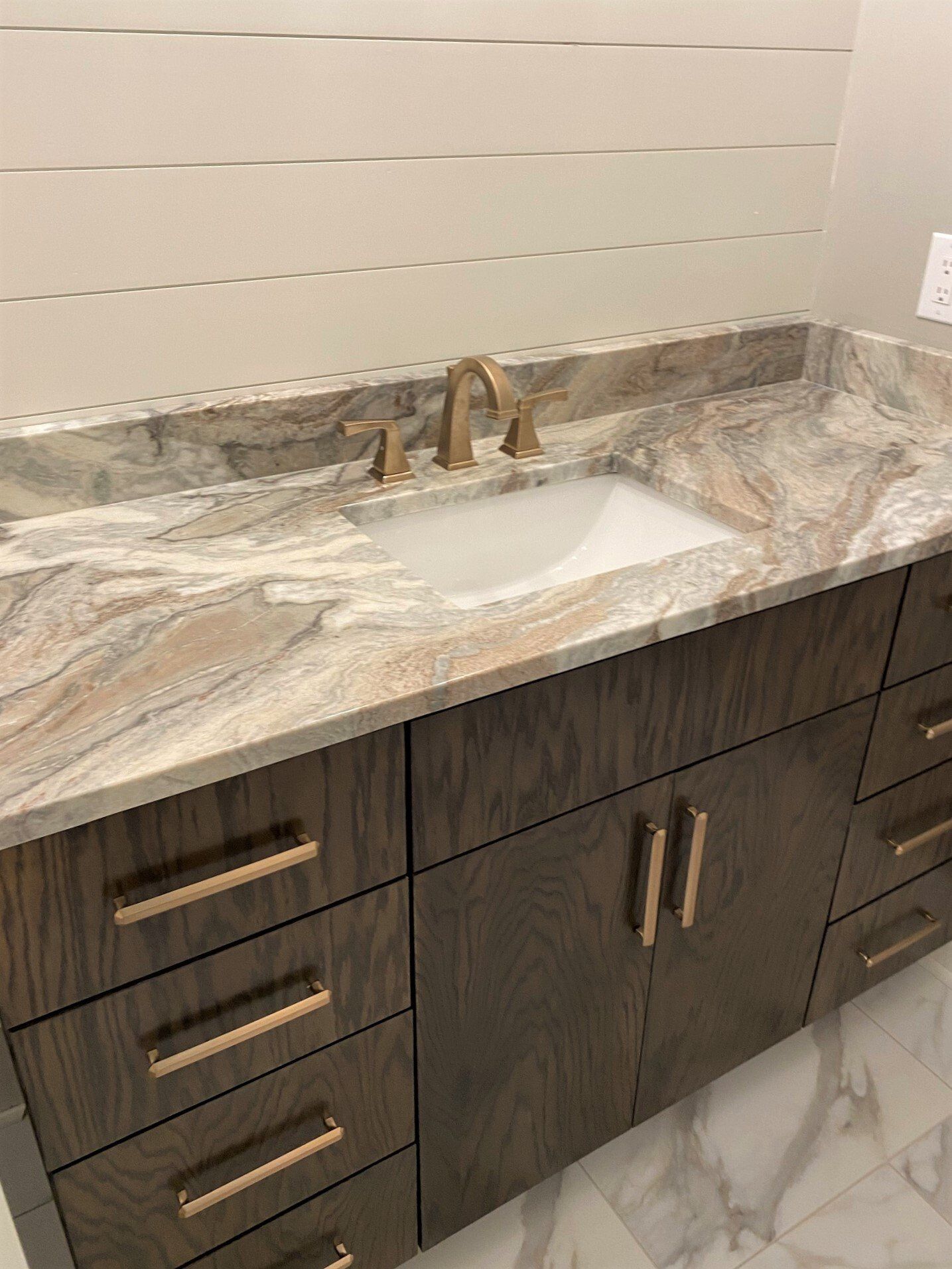 A bathroom sink with a marble counter top and wooden cabinets.