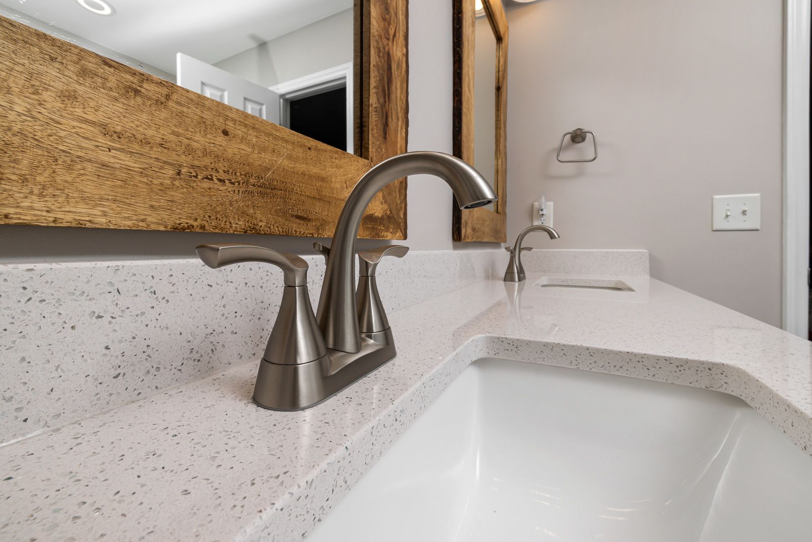 Bathroom vanity with brushed nickel faucet, white sink, and countertop; a wooden framed mirror is above.