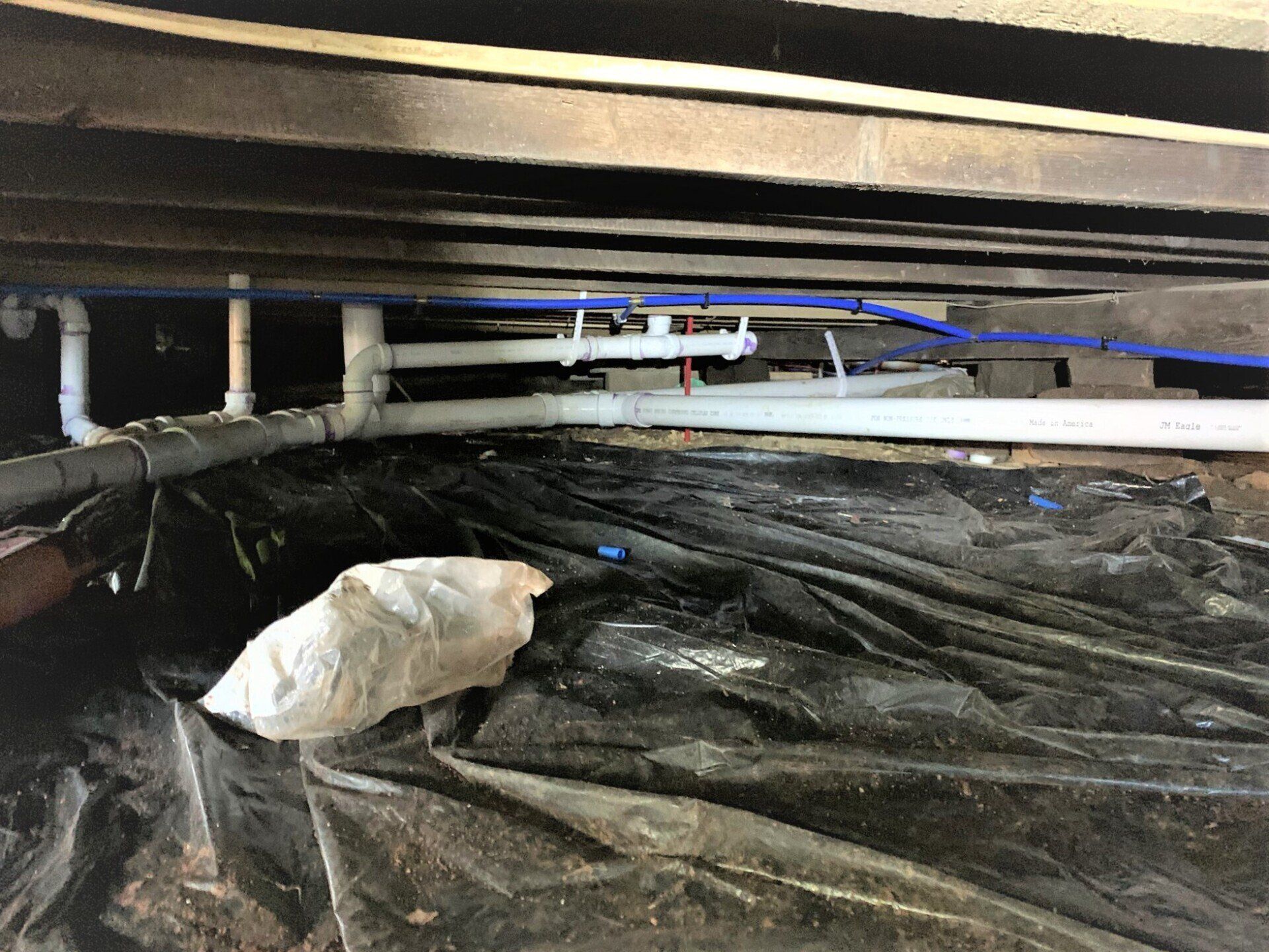 A person is working under a wooden floor in a basement.