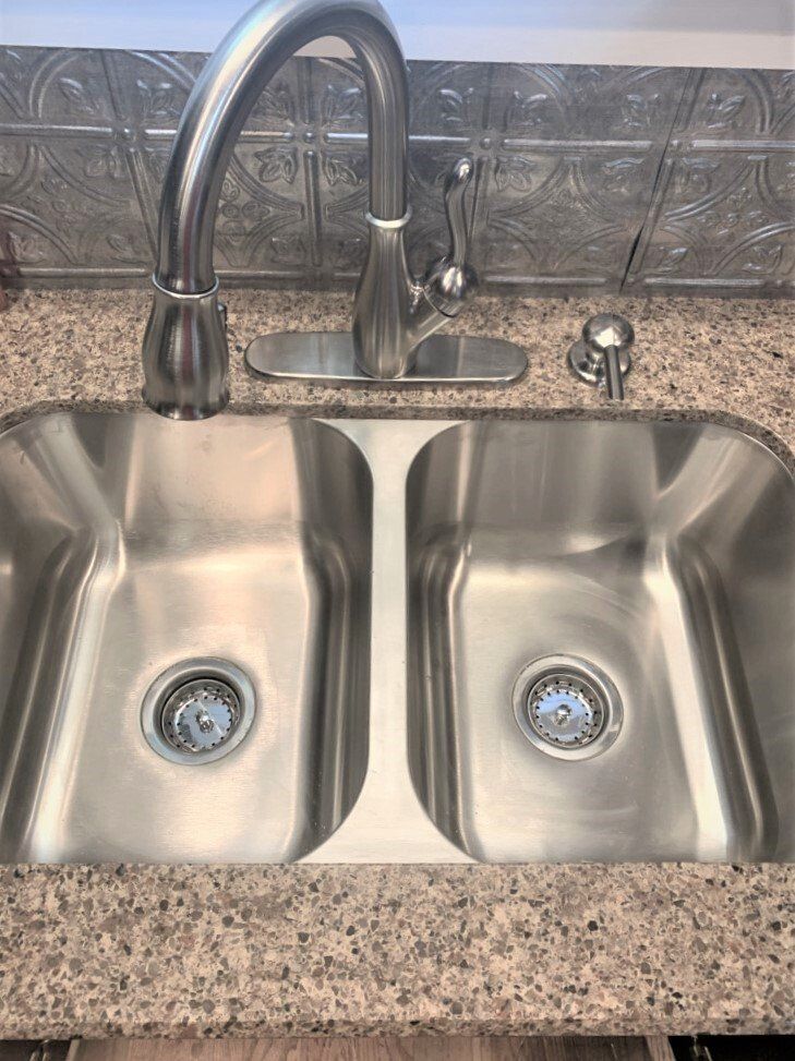A stainless steel kitchen sink with two sinks and a faucet on a granite counter top.