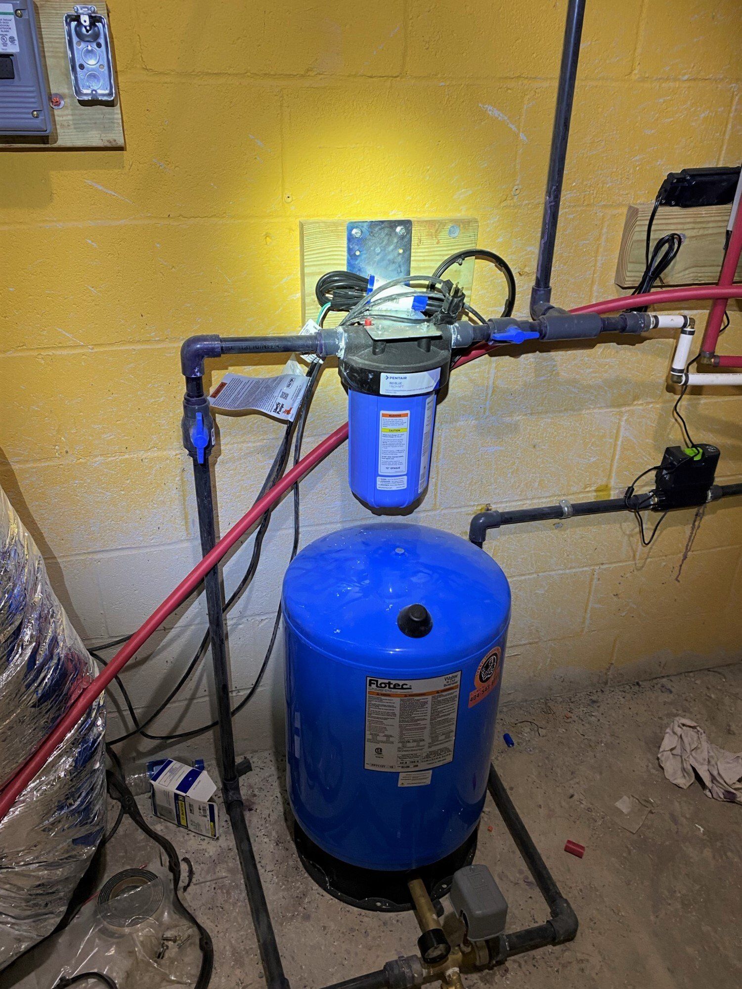 A blue water tank is sitting in a basement next to a yellow wall.