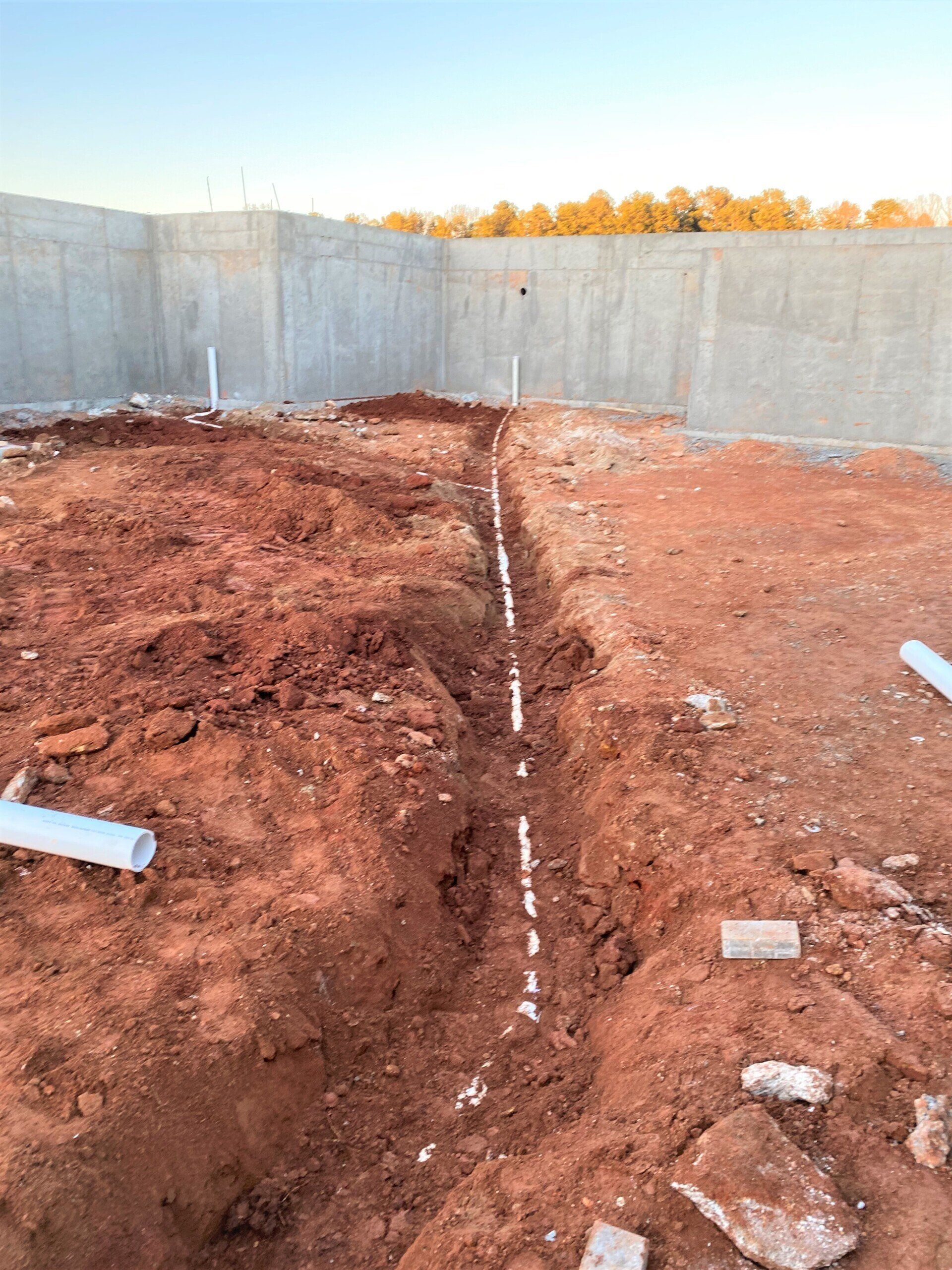 A drain pipe is being installed in the dirt in front of a concrete wall.