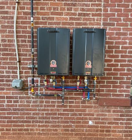 Two black water heaters are mounted on a brick wall.