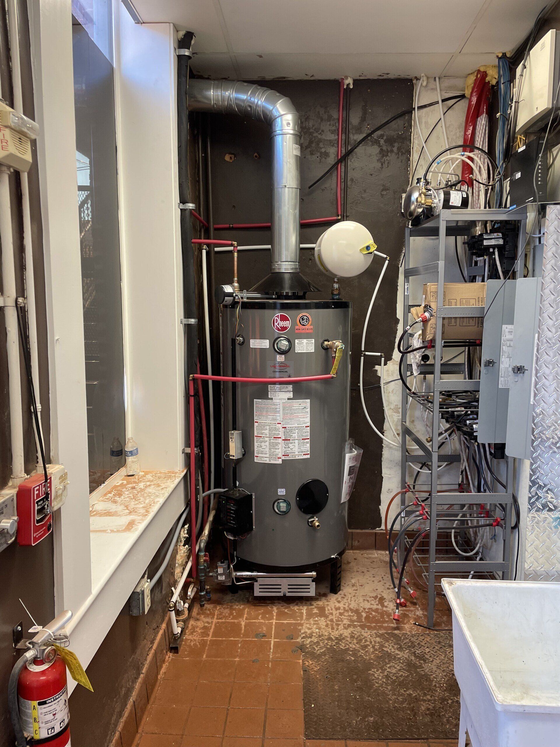 A water heater is sitting in a room next to a fire extinguisher.