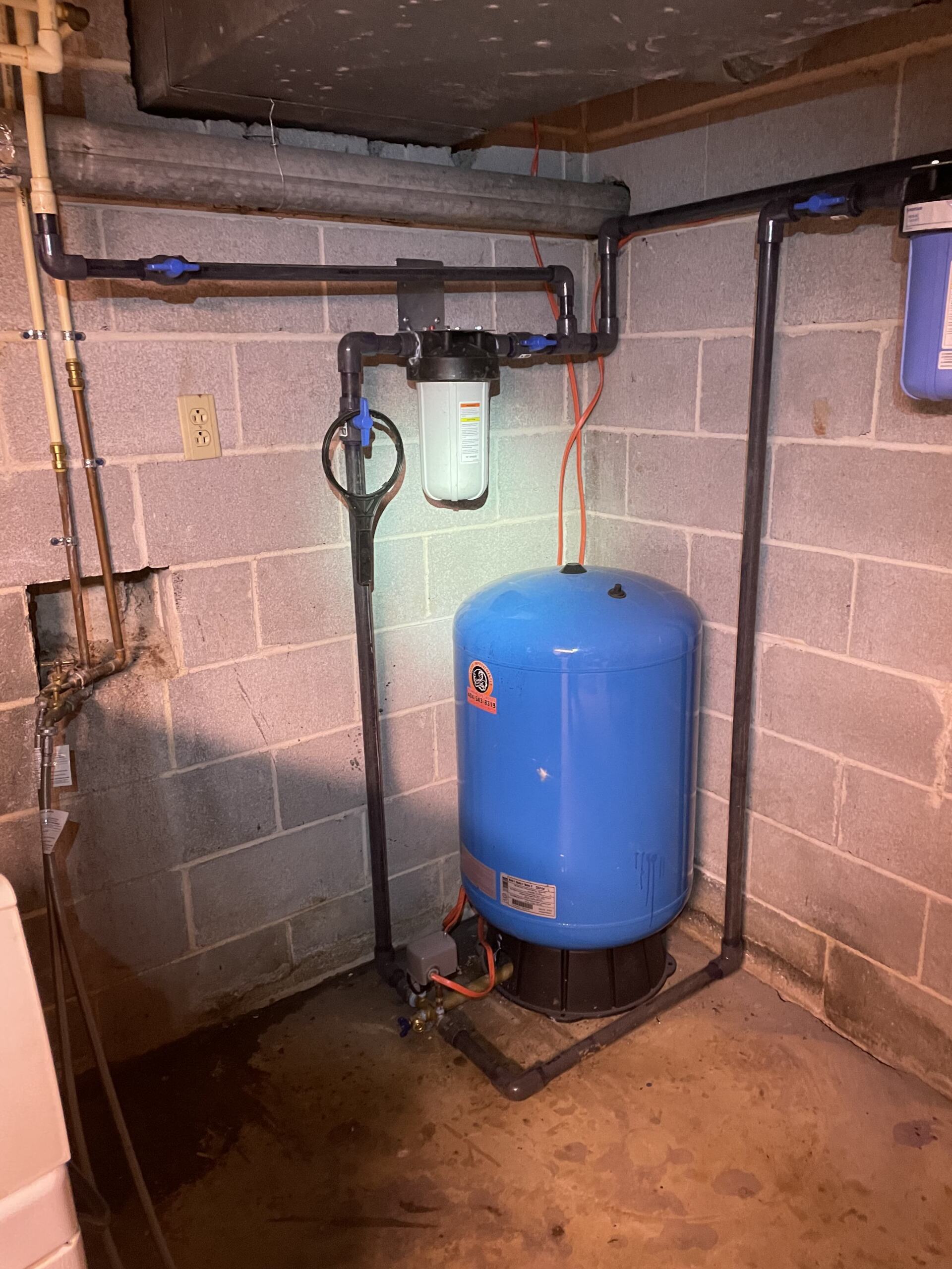 A blue water tank is sitting in a basement next to a brick wall.