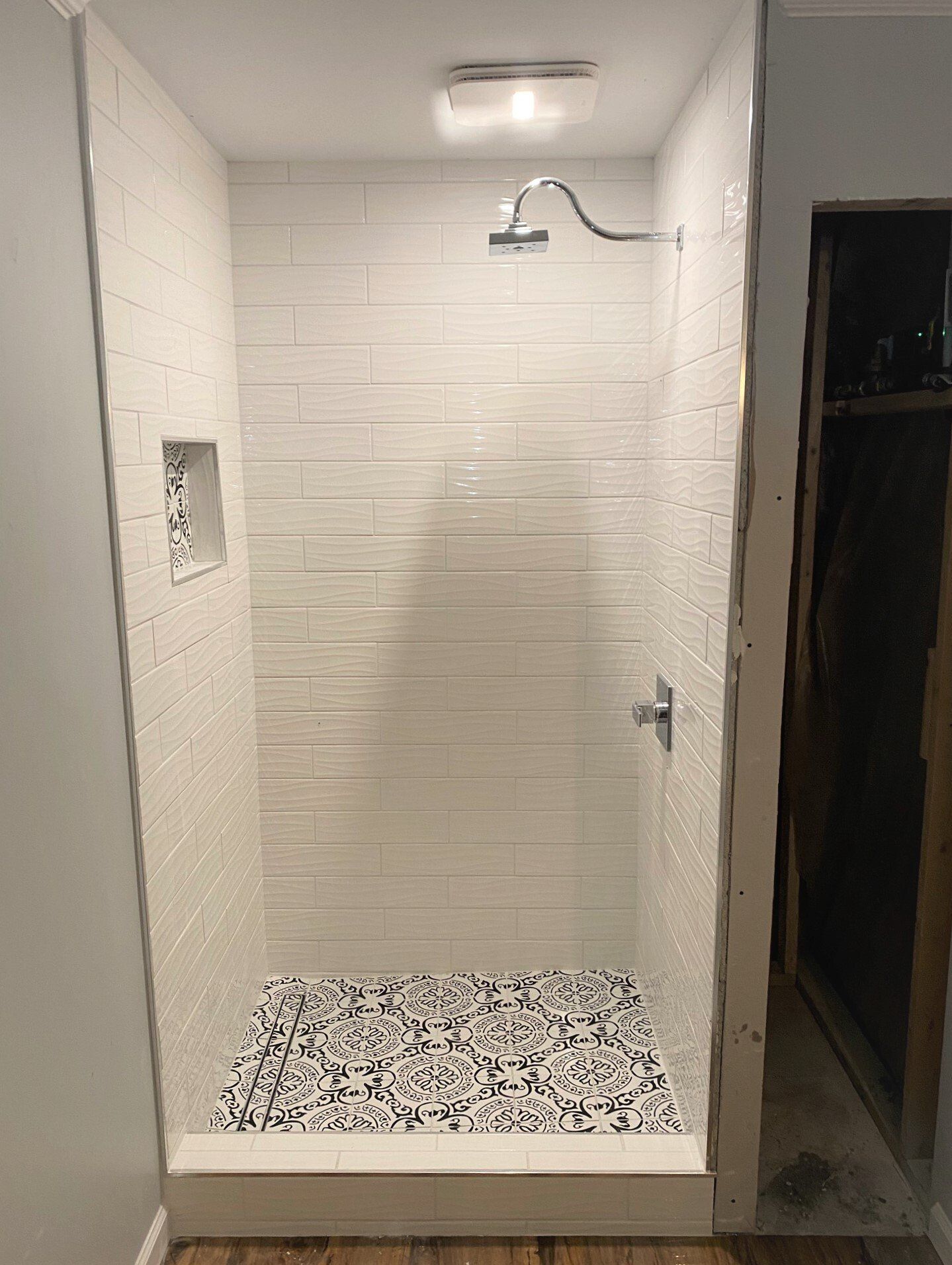A shower with white tiles and a black and white tile floor.