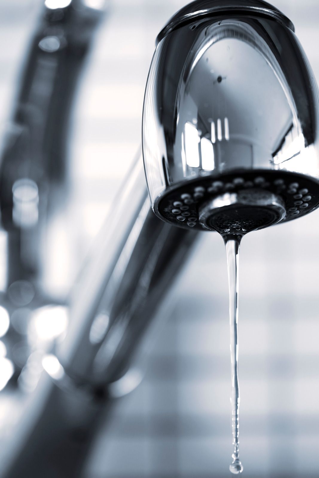 A close-up of a modern, chrome kitchen faucet with a single, thin stream of water dripping from the aerator.