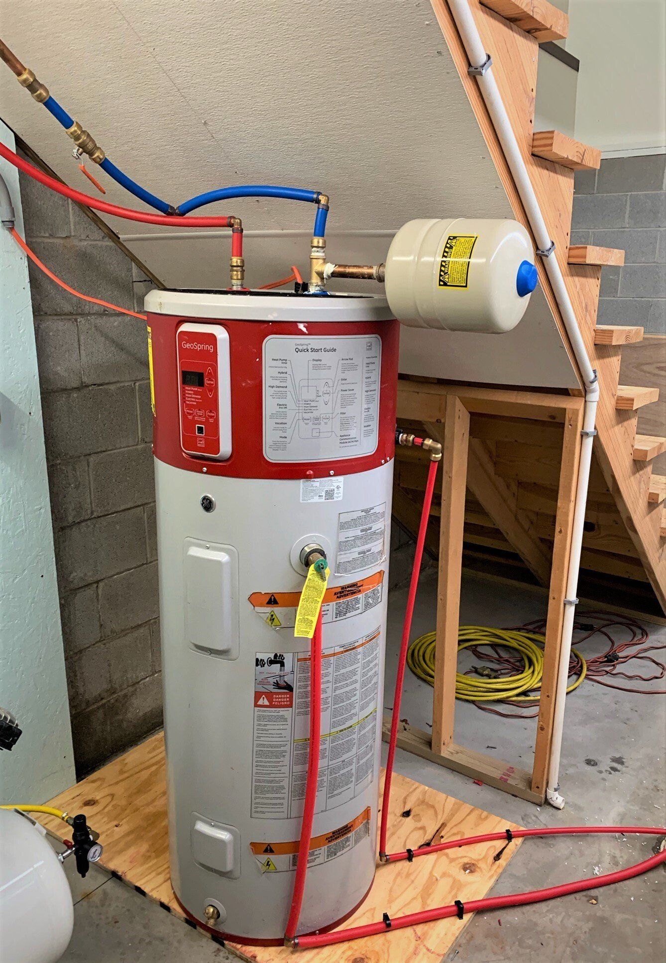 A water heater is sitting on a wooden floor next to a staircase.
