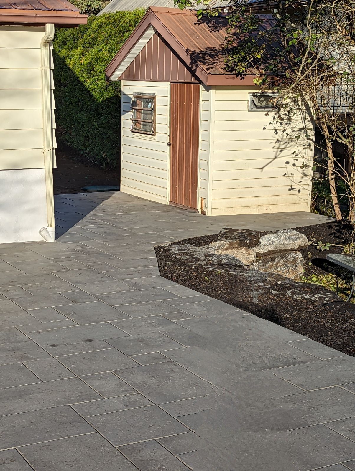 Un hangar blanc avec une porte marron se trouve à côté d'une maison blanche.