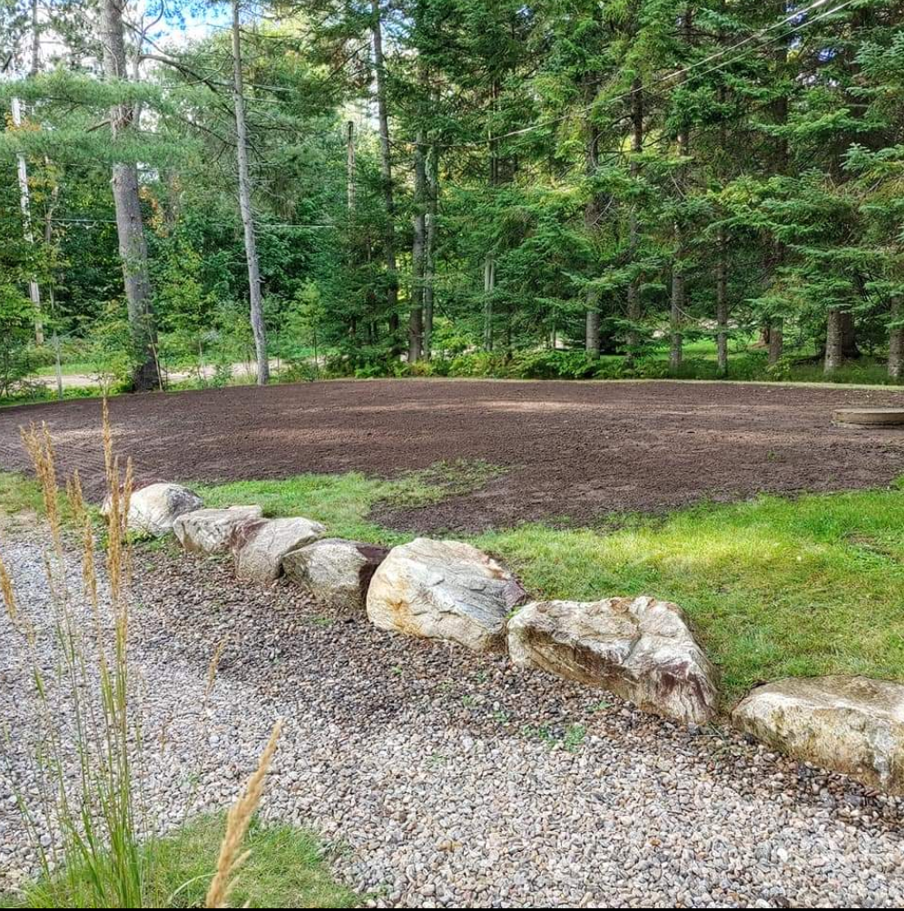 Une paroi rocheuse entoure une zone de gravier au milieu d'une forêt.