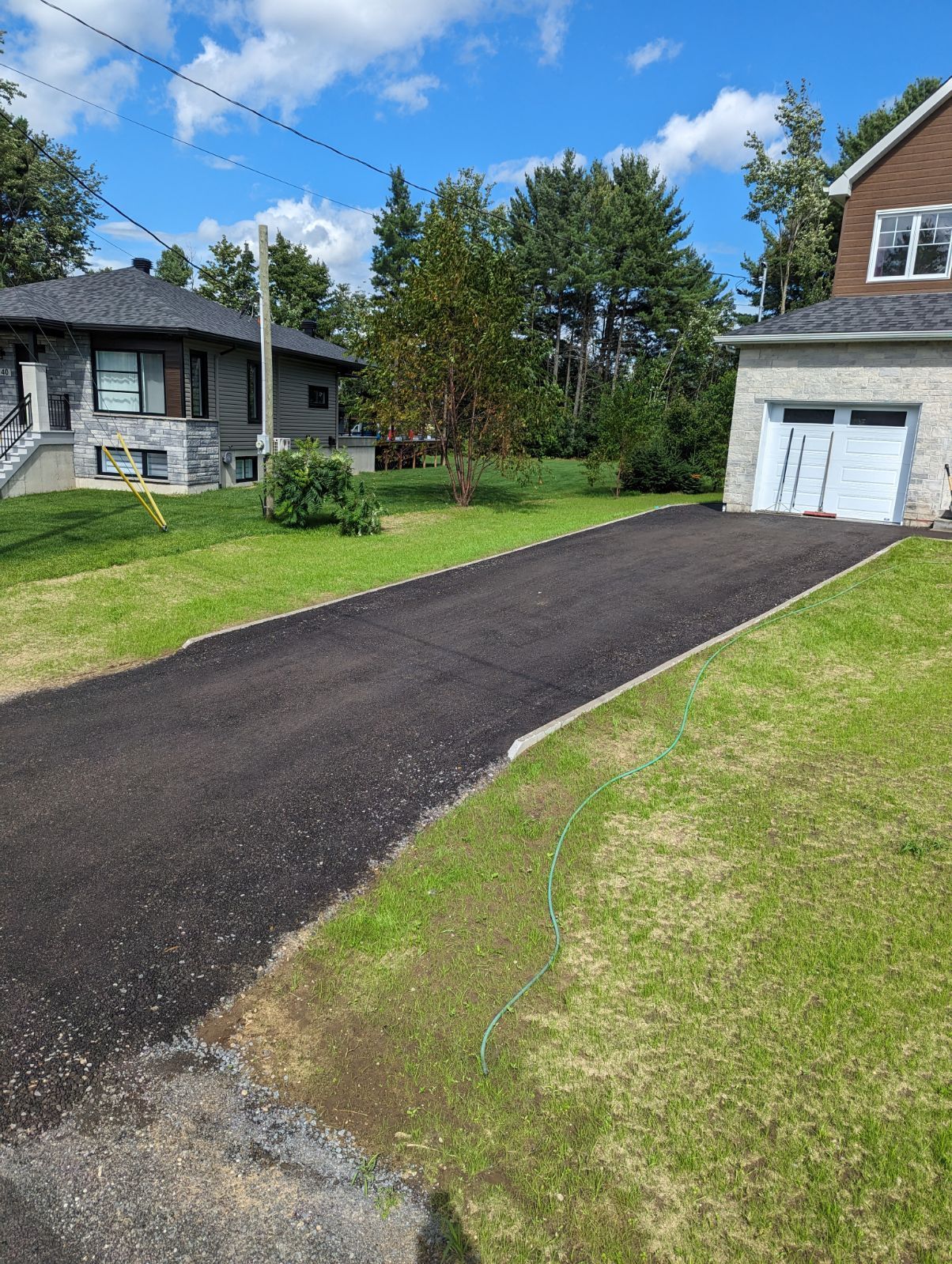 Une allée menant à une maison avec garage et une maison en arrière-plan.