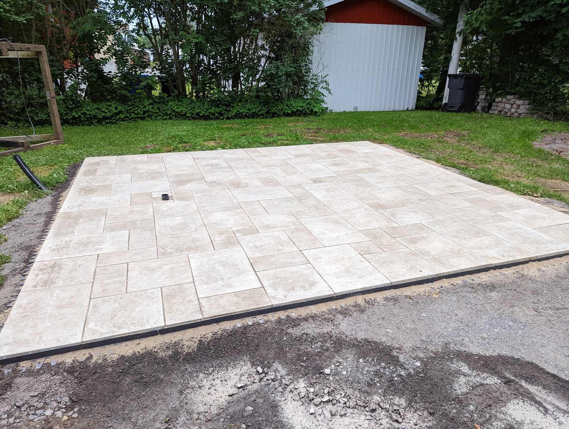 Un patio est en cours de construction dans une cour arrière avec un cabanon en arrière-plan.