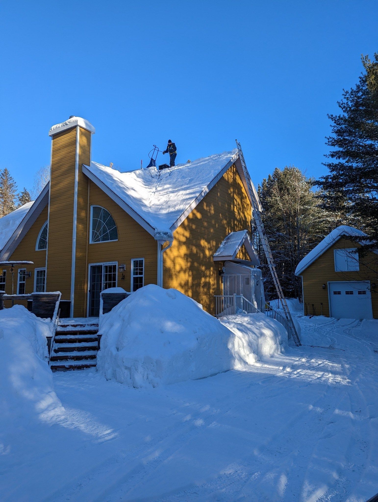 Une maison jaune est couverte de neige par une journée ensoleillée.