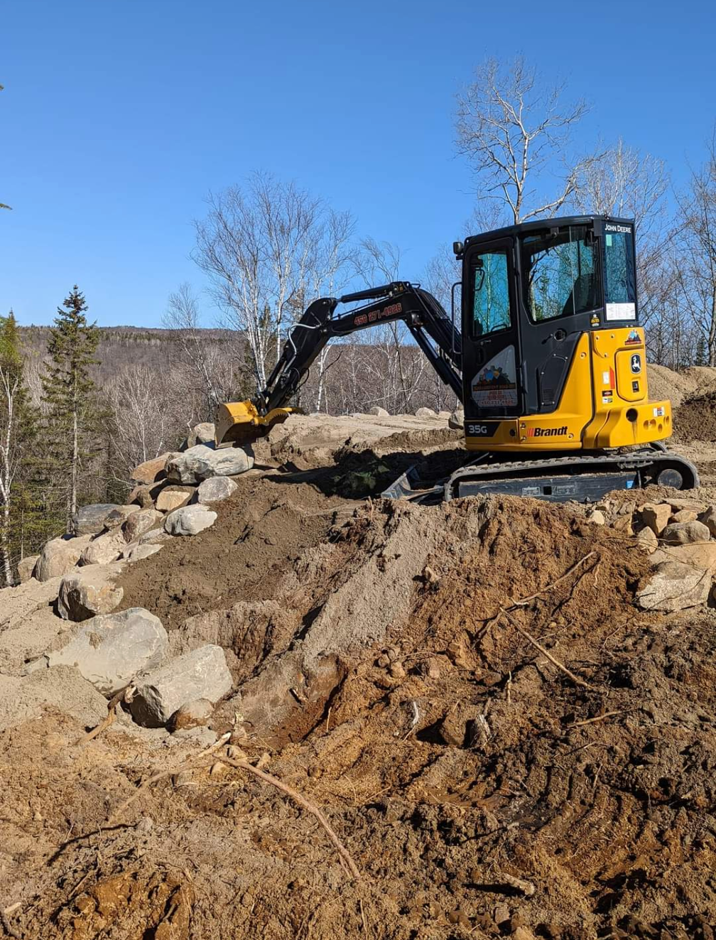 Une excavatrice jaune travaille sur un tas de terre et de roches.