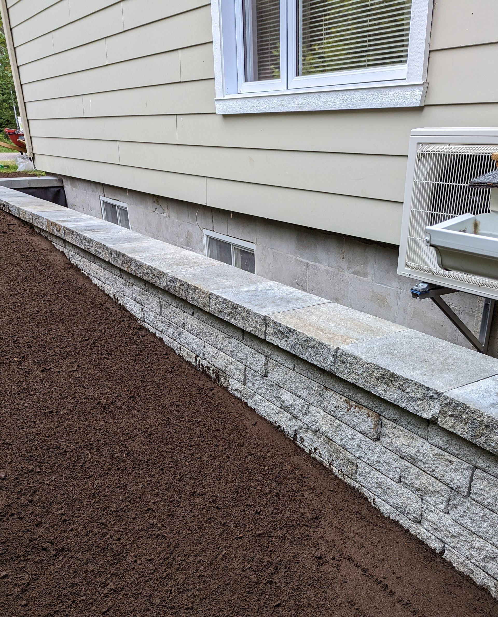 Un mur de pierre est en construction devant une maison.